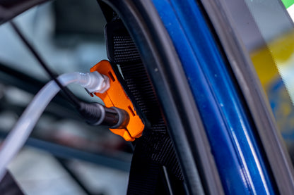 Close-up of an orange and black tire hydration connector connected to a translucent hose inside a blue race car