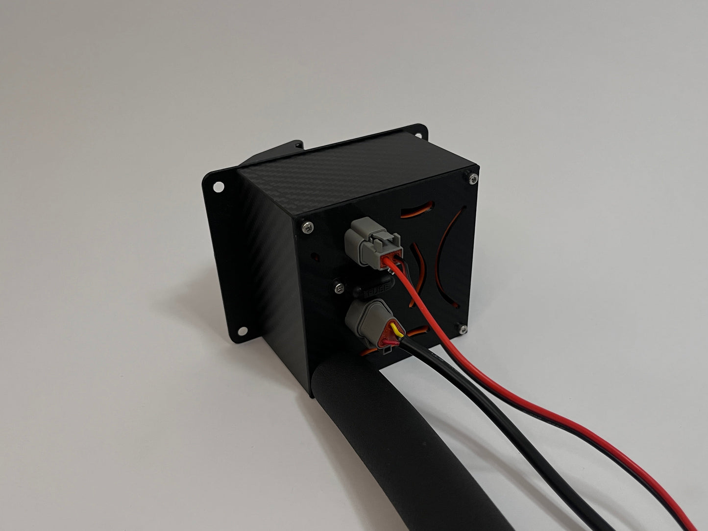 rear of racing hydration unit laying on the side showing a black carbon fiber unit with 2 Deutsch connectors on the rear and a black insulated tube on a white background
