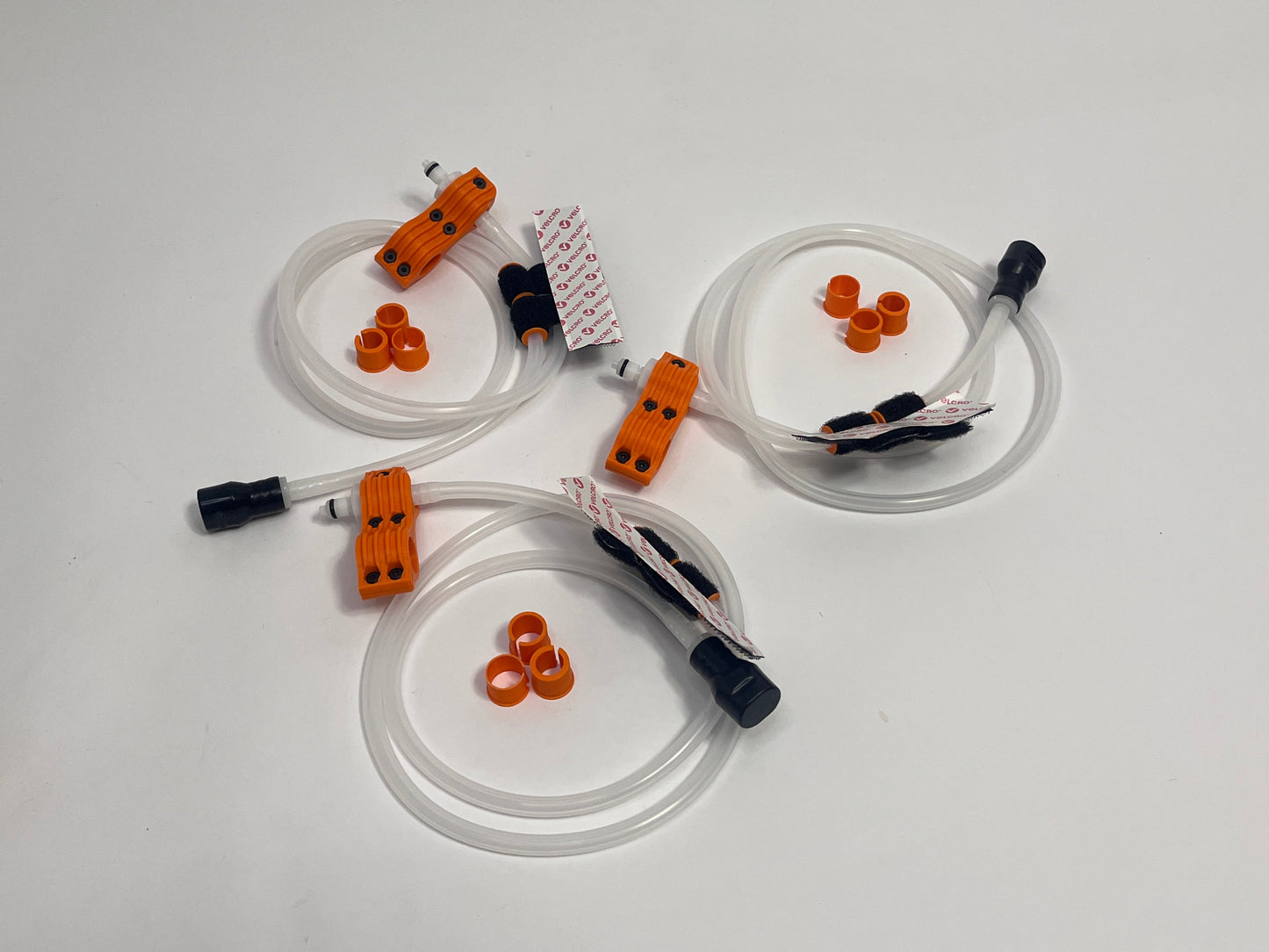 three driver side racing driver drinking kits showing per set orange dry break fitting holder, 1m silicone tubing connected to it with 3 spacers shown loosely. black silicone bite valve is connected to the tube and velcro positioners connected to the tubing on a light gray background