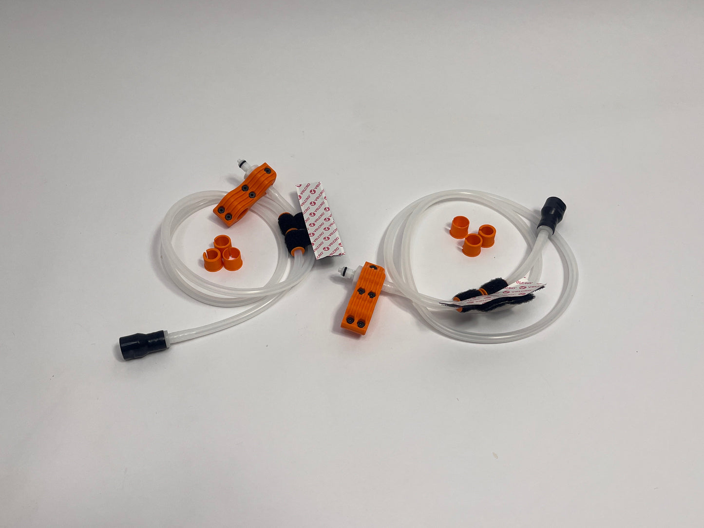 two driver side racing hydration kits showing per set orange dry break fitting holder, 1m silicone tubing connected to it with 3 spacers shown loosely. black silicone bite valve is connected to the tube and velcro positioners connected to the tubing on a light gray background