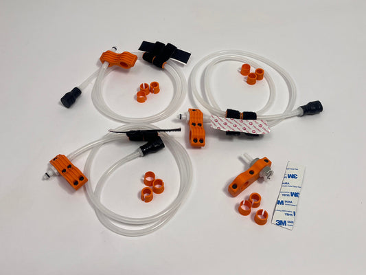 three driver side motorsport helmet drinking kits showing per set orange dry break fitting holder, 1m silicone tubing connected to it with 3 spacers shown loosely. black silicone bite valve is connected to the tube and velcro positioners connected to the tubing. also a car side connector in orange shown with dry break fitting installed, 3m backed rubber and 3 orange radio plug spacers on a light gray background