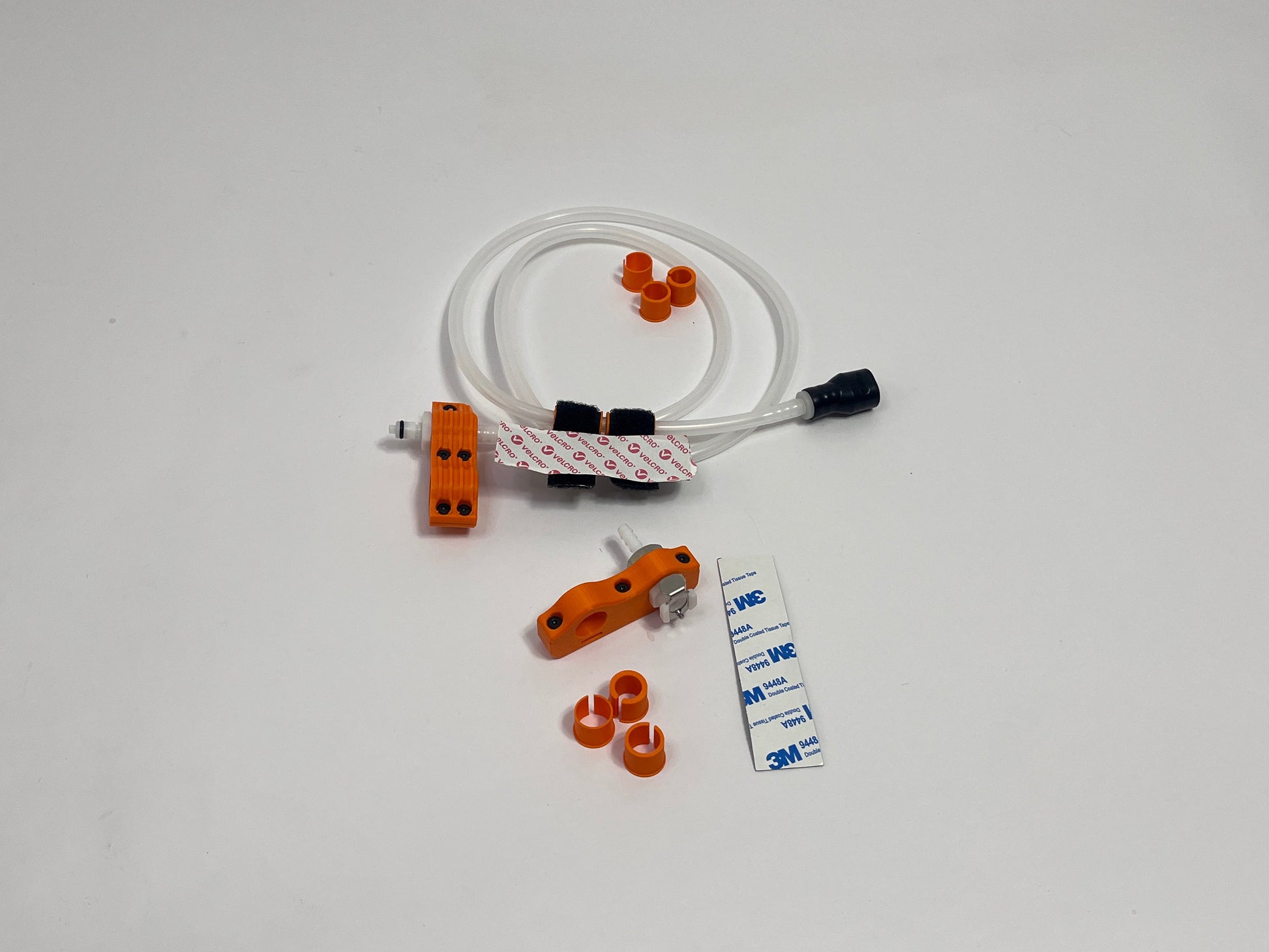 a driver side racing hydration kits showing per set orange dry break fitting holder, 1m silicone tubing connected to it with 3 spacers shown loosely. black silicone bite valve is connected to the tube and velcro positioners connected to the tubing. also a car side connector in orange shown with dry break fitting installed, 3m backed rubber and 3 orange radio plug spacers on a light gray background